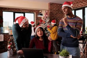 multiethnic-team-coworkers-using-laptop-christmas-working-project-office-decorated-with-festive-ornaments-xmas-tree-people-with-santa-hat-doing-teamwork-holiday_482257-47171